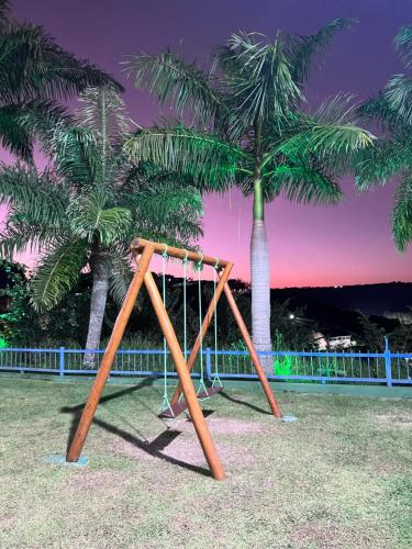 a swing set in front of two palm trees at Lindo Apartamento no Condomínio Alto da Serra Villas de Bananeiras in Bananeiras