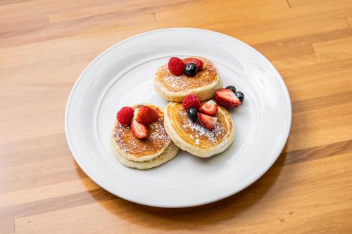 a white plate with three pancakes with strawberries on it at The Fullerton Hotel Sydney in Sydney