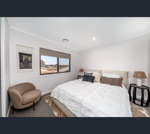 a white bedroom with a bed and a chair at Brand New Luxury Abode on Shaw in Wagga Wagga