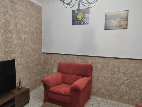una silla roja sentada en una sala de estar junto a una TV en Casa RISAN, en Cañete la Real