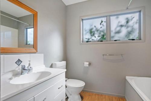 a bathroom with a sink and a toilet and a mirror at Family Harmony - Waihi Beach Holiday Home in Waihi Beach