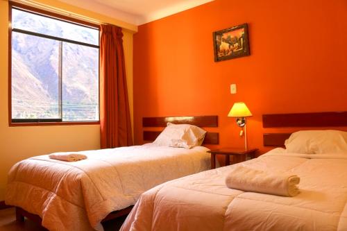 2 camas en una habitación con paredes de color naranja y ventana en Inka's Haven Hotel en Ollantaytambo