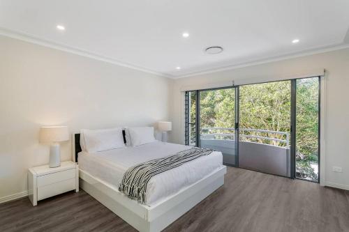 a white bedroom with a bed and a large window at DY008 - 3 bedroom townhouse - Dee Why in Sydney