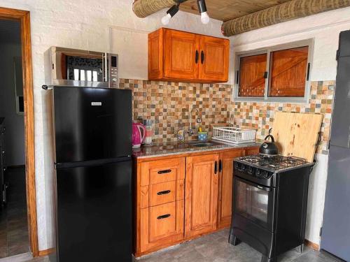 a kitchen with a black refrigerator and wooden cabinets at Villa Serrana Cabaña Tata Ruben y Olga 2dormitorios in Villa Serrana