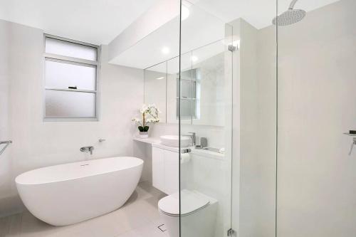 a white bathroom with a tub and a glass shower at HARIS - Modern 2BR Apartment with Views in Sydney
