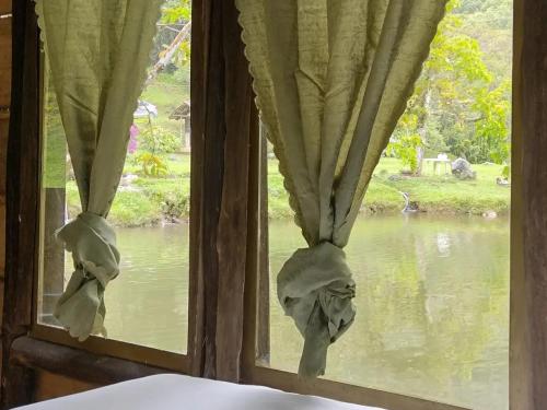 a window with curtains with a view of a river at Sapiens house cabaña del lago clásica in Cali