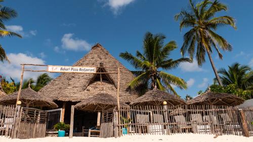 a building with straw umbrellas and palm trees on a beach at BONDENI BEACH HOUSE in Jambiani