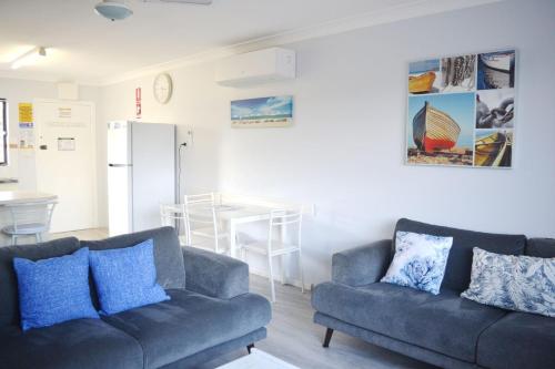 a living room with two blue couches and a kitchen at Village Centre 6 in South West Rocks