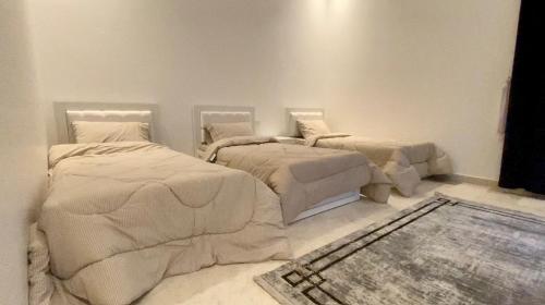 two beds in a white room with a rug at La Vida Inn Quriyat 