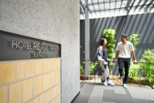 un hombre y una mujer caminando delante de un edificio en Hotel Resol Trinity Kanazawa en Kanazawa