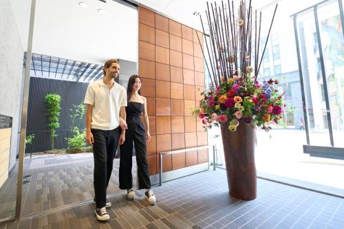 a man and a woman standing next to a vase of flowers at Hotel Resol Trinity Kanazawa in Kanazawa