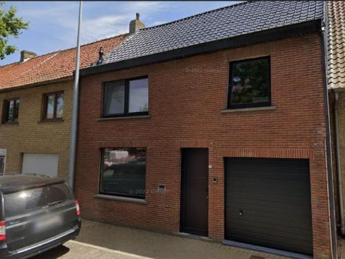 een bakstenen huis met twee garagedeuren en een auto geparkeerd aan de voorkant bij Maison Beau in Veurne