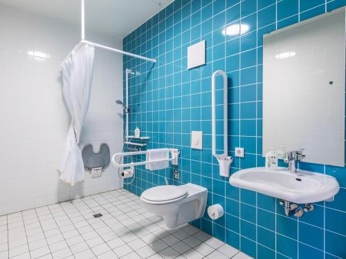 W wyłożonej niebieskimi kafelkami łazience znajduje się toaleta i umywalka. w obiekcie B&B Hotel Rosenheim w mieście Rosenheim