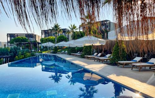 a swimming pool with chairs and umbrellas next to a building at Allium Bodrum Resort & Spa in Yalıkavak