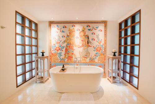 a bath tub in a bathroom with a painting on the wall at Ramayana Suites and Resort in Kuta