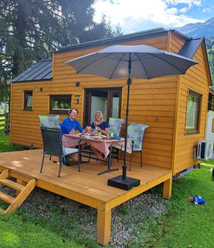 a man and woman sitting at a table with an umbrella at Tiny House Waldschmied 1 in Latzendorf