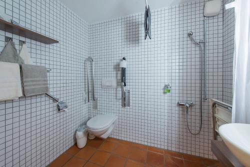 a white tiled bathroom with a toilet and a shower at Hotel Glocke in Reckingen - Gluringen