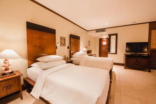 a hotel room with four beds and a flat screen tv at Ramayana Suites and Resort in Kuta