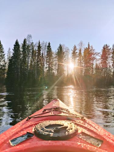 a red kayak on the water with the sun in the background at Långforsen Glamping & Lapland Experience in Haparanda