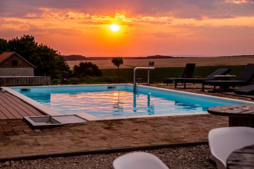 a swimming pool with a sunset in the background at Nagypince Borhotel Wine and Spa in Böhönye
