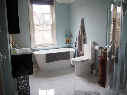 a bathroom with a tub and a toilet and a window at Stunning property overlooking local park in London