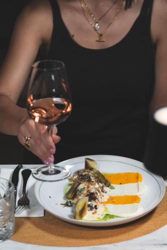 a woman holding a glass of wine next to a plate of food at Zeus Village Resort - Adults Only in Kato Daratso