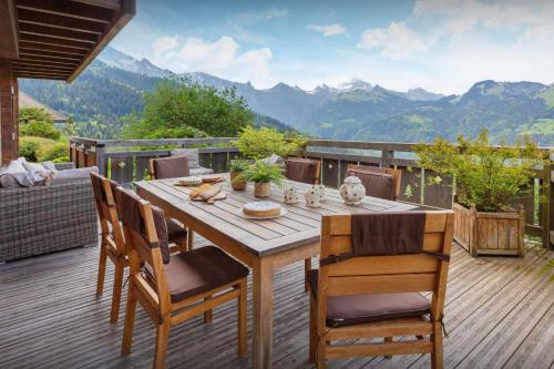 una mesa de madera y sillas en una terraza con montañas en Chalet Isatys - OVO Network, en Manigod