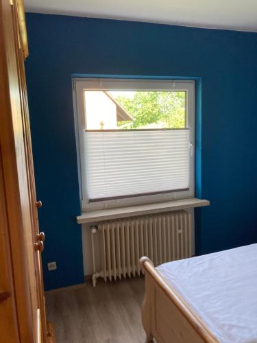 a bedroom with a blue wall and a window at Helles Ferienhaus Storchenblick in Buchholz Aller