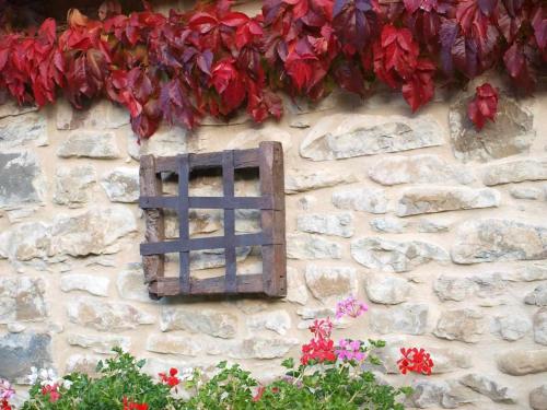 a stone wall with a window and red flowers at Casapirineos Apartamentos in Ulle