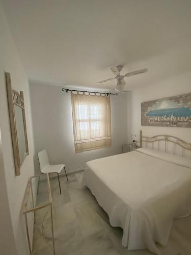 a white bedroom with a bed and a chair at Casitasmanoli Conil plaza Huerta de enmedio in Conil de la Frontera