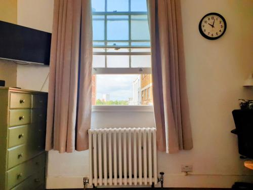 a window with a radiator and a clock on a wall at Charming Studio Sleeps 2 - Kentish Town NWLondon in London