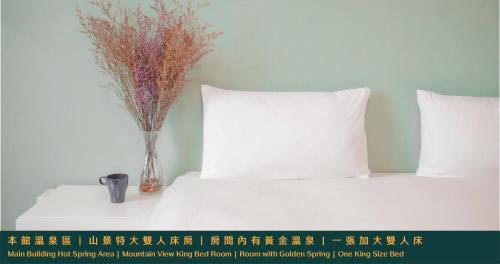 a white bed with a vase of flowers on a table at Ruixiong Hotspring Hotel in Ruisui