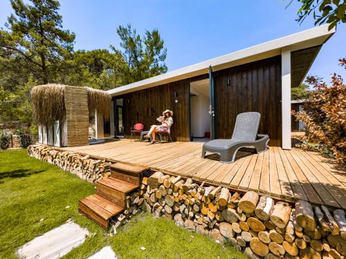 a woman sitting on a wooden deck next to a house at Mossa Afkule Kayaköy in Fethiye