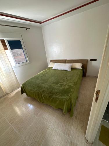 een slaapkamer met een bed met een groen dekbed en een raam bij Apartement pret de la gare train in Nador