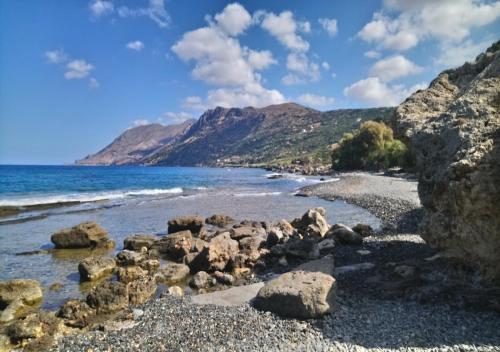 a beach with rocks and the ocean and mountains at Kleio Studios in Ravdhoúkha