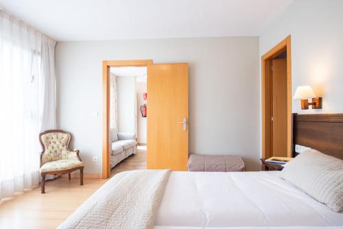 a bedroom with a white bed and a chair at Apartamentos Aldea del Puente in Cangas de Onís