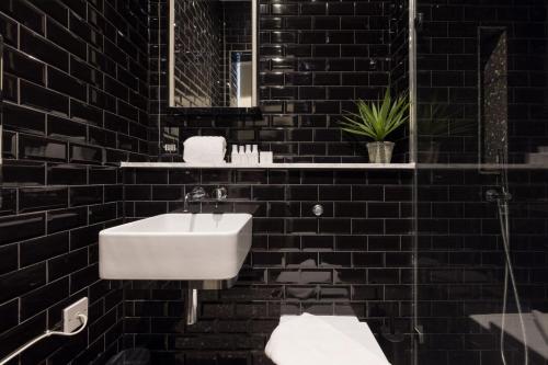 a black tiled bathroom with a sink and a mirror at The Notting Hill Apartments By Hok Living - Nh3 in London
