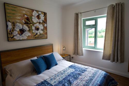 a bedroom with a bed with blue pillows and a window at Tring Grange Cottage in Wigginton