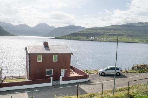 a house with a car parked next to a body of water at The Cozy red house with Amazing sea view in Morskranes