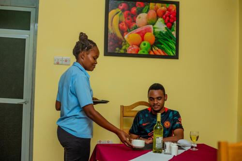a woman standing next to a man sitting at a table at Randa Cottages Moshi in Kirua