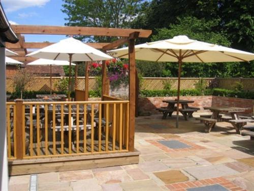 un patio avec deux parasols, une table et des bancs dans l'établissement The Plume of Feathers, à Farnham