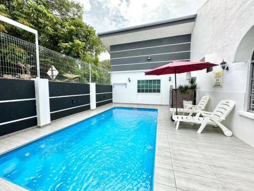 a swimming pool with chairs and an umbrella on a patio at H&H 1 Guest House in Malacca