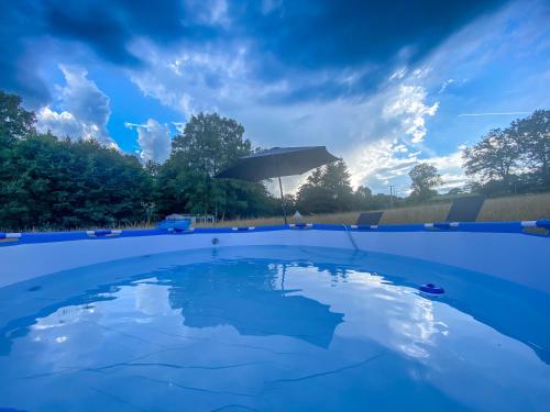 une piscine bleue avec un parasol et des nuages dans le ciel dans l'établissement Mini-Glamping en Auvergne, à Sainte-Christine