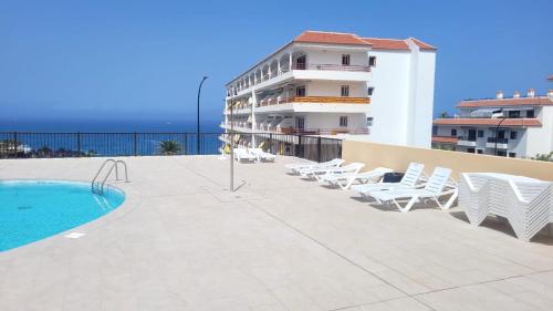 a swimming pool with lounge chairs and a building at Oceanfront Beach Apartment la Arena in Puerto de Santiago