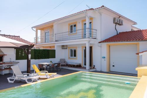 a villa with a swimming pool in front of a house at Retiro da Atafona Beach Pool House White 