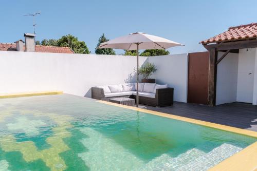a swimming pool with an umbrella next to a house at Retiro da Atafona Beach Pool House White in Monte