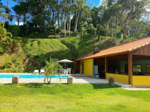 a yellow house with a pool and a table and an umbrella at Chalé Hibisco Amarelo in Juquitiba