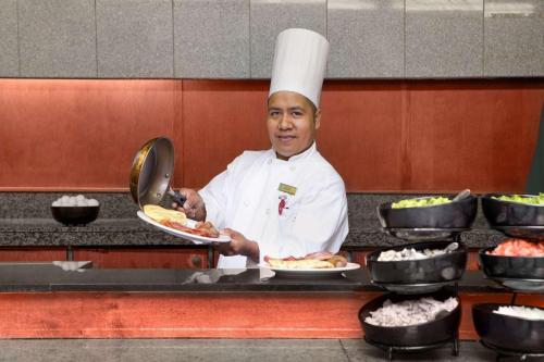 a chef standing in a kitchen holding plates of food at Embassy Suites by Hilton Chicago O'Hare Rosemont in Rosemont