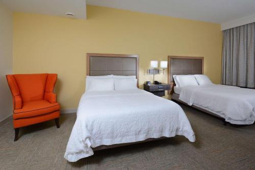 a hotel room with two beds and an orange chair at Hampton Inn Charlotte North Lake Norman in Cornelius
