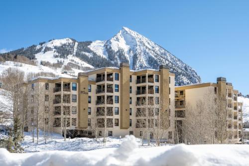 um edifício na neve com uma montanha ao fundo em The Plaza Condominiums by Crested Butte Mountain Resort em Mount Crested Butte